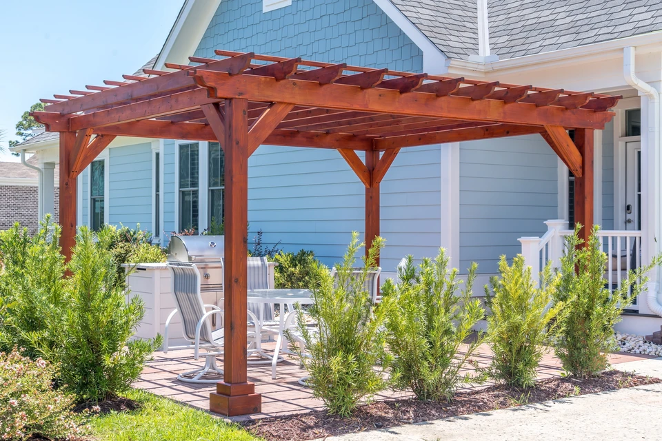 Terrasse extérieure branchée structure ombragée de pergola en bois foncé, auvent et toit-terrasse, table à manger blanche, chaises blanches, grill en métal entouré de paysages dans un quartier américain de luxe
