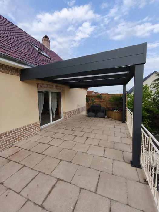 Terrasse extérieure en dallage calcaire beige, équipée d'une pergola bioclimatique aluminium anthracite à lames orientables