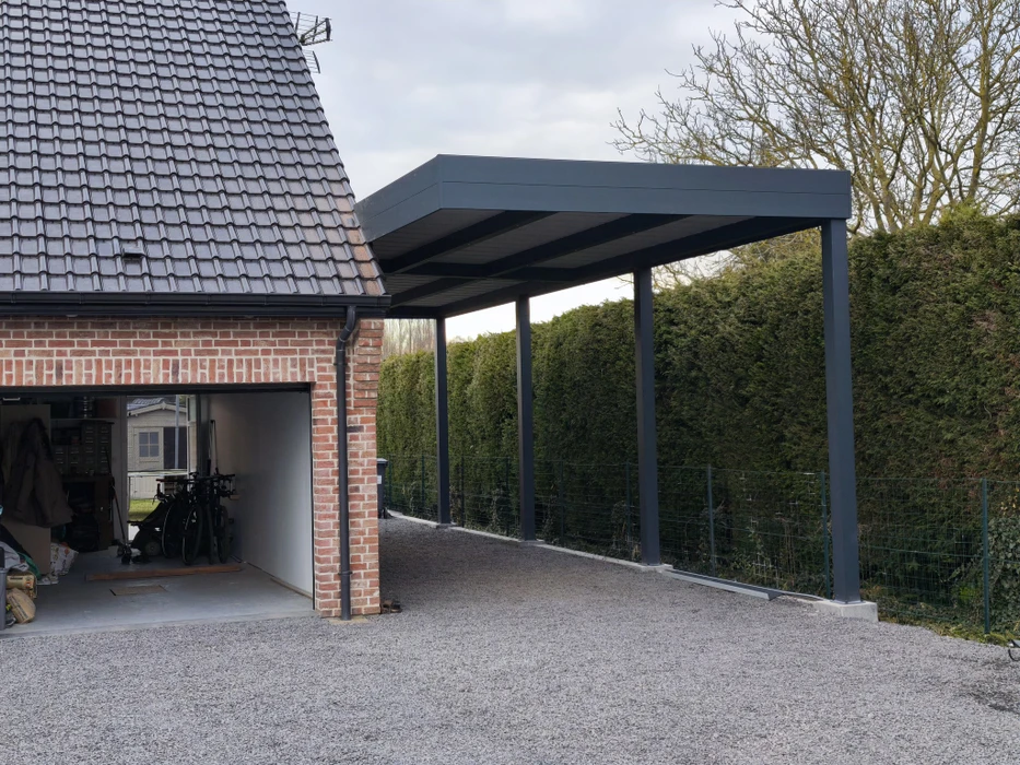 Carport métallique moderne adossé à un garage en briques rouges, toiture tuiles grises