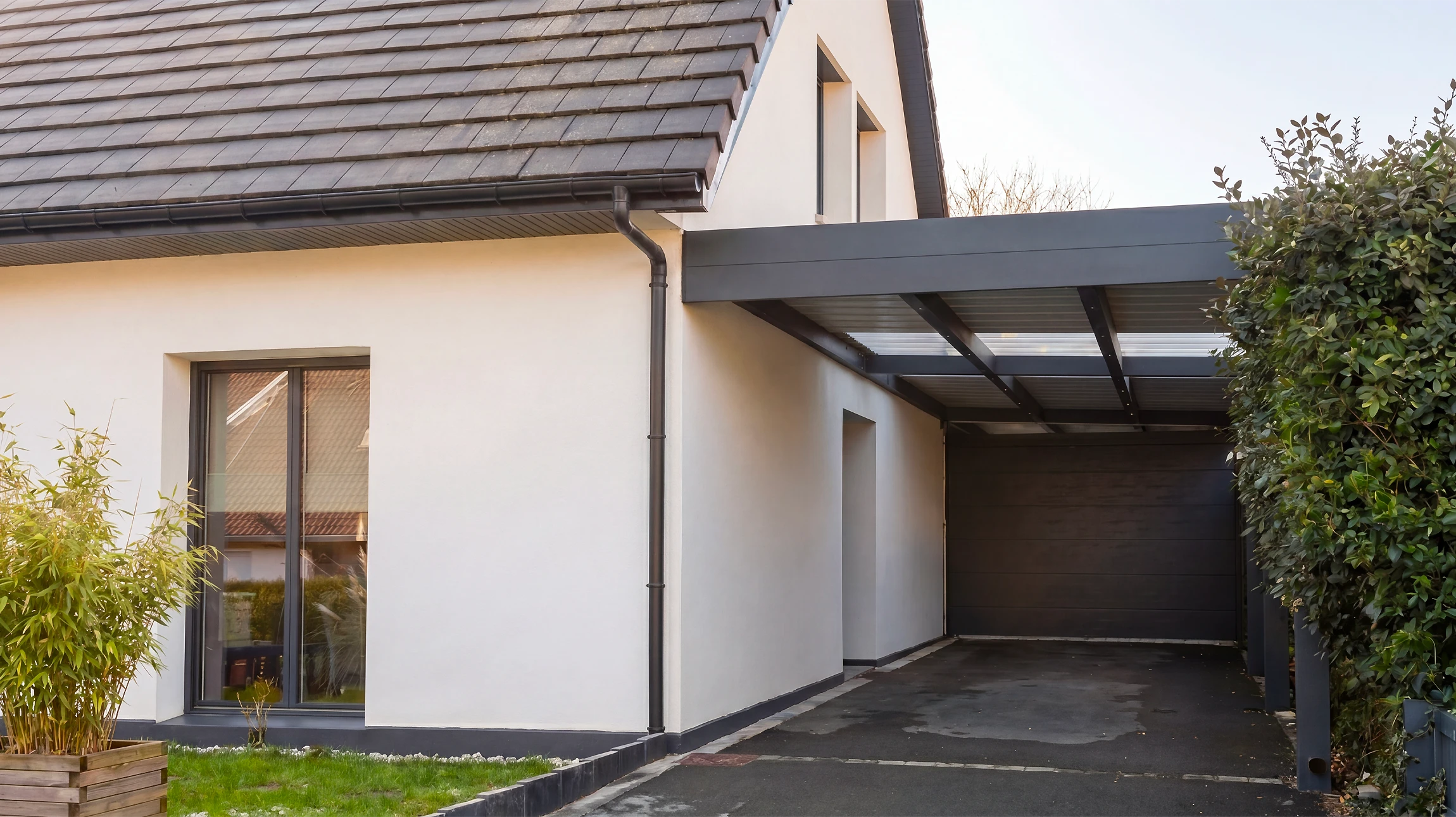 Carport adoss&eacute; &agrave; une maison individuelle moderne, fa&ccedil;ade enduit blanc, toiture tuiles ardoise