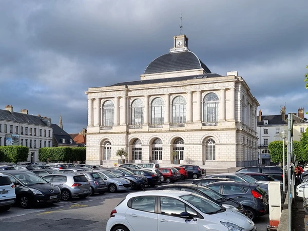 Vue a&eacute;rienne ou perspective d'une petite ville fran&ccedil;aise de la r&eacute;gion des Hauts-de-France montrant l'urbanisme local avec maisons r&eacute;sidentielles traditionnelles et modernes, rues pav&eacute;es ou routes r&eacute;gionales, points de rep&egrave;re architecturaux locaux comme une &eacute;glise ou b&acirc;timents commerciaux, entour&eacute;s de zone rurale avec champs ou verdure. La photo doit capturer l'essence g&eacute;ographique et administrative d'une commune picarde, en lumi&egrave;re naturelle claire, sans texte ou overlay visible.