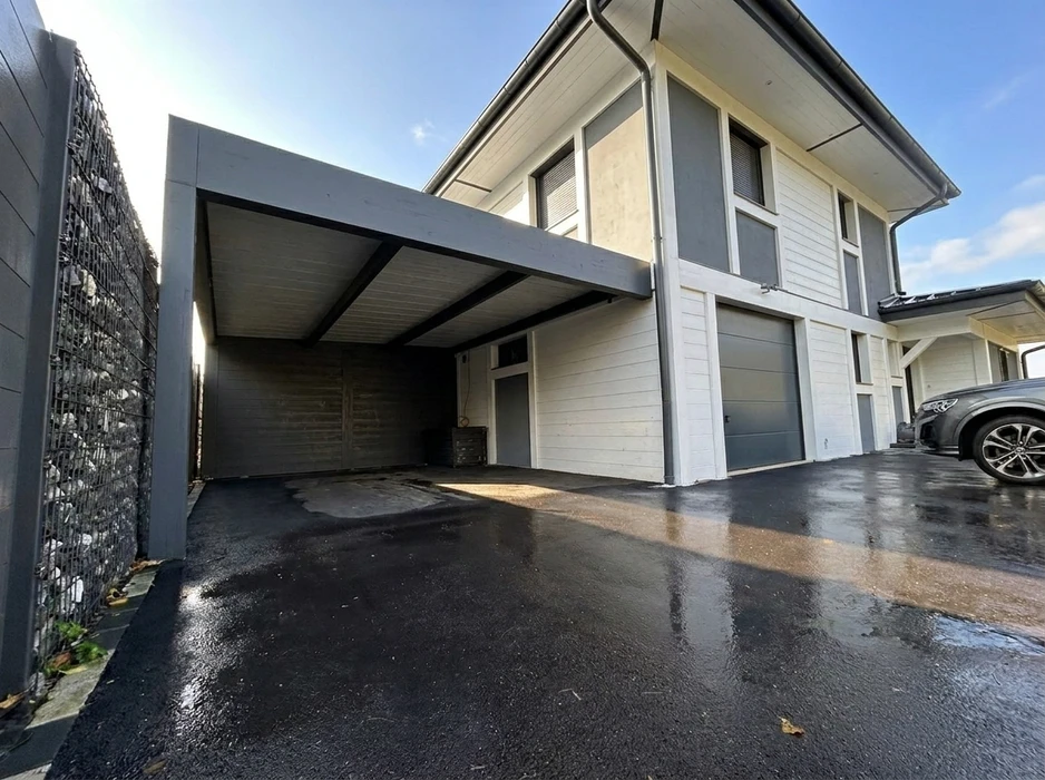 Carport moderne accolé à une maison en briques, toiture plate en acier anthracite, structure métallique apparente