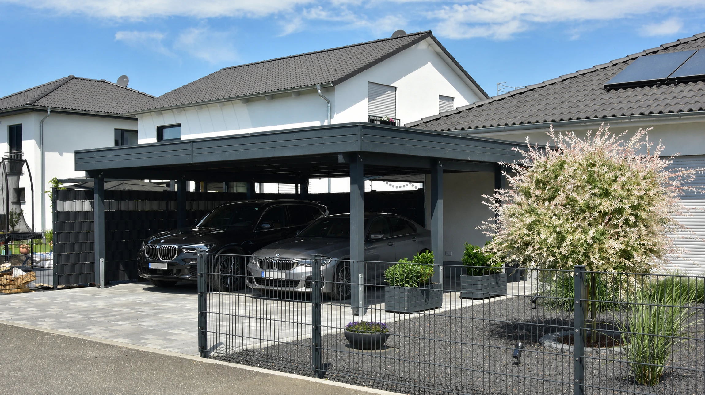 Voiture blanche garée sous un carport moderne en structure métallique avec toiture polycarbonate translucide